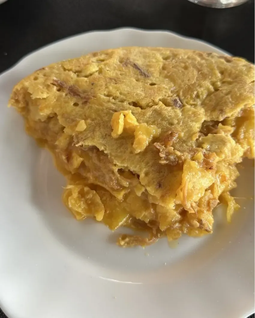 Una porción de tortilla amarilla o frittata en un plato blanco.
