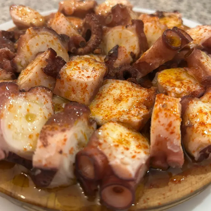 Primer plano de pulpo en rodajas sazonado en un plato, rociado con aceite y hojuelas de pimiento rojo.