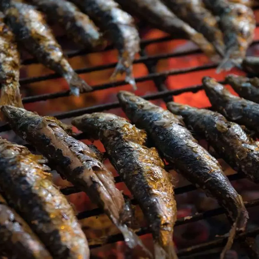 Pescado a la parrilla chisporroteando sobre una rejilla de alambre sobre brasas calientes, con la piel carbonizada y un glaseado brillante.