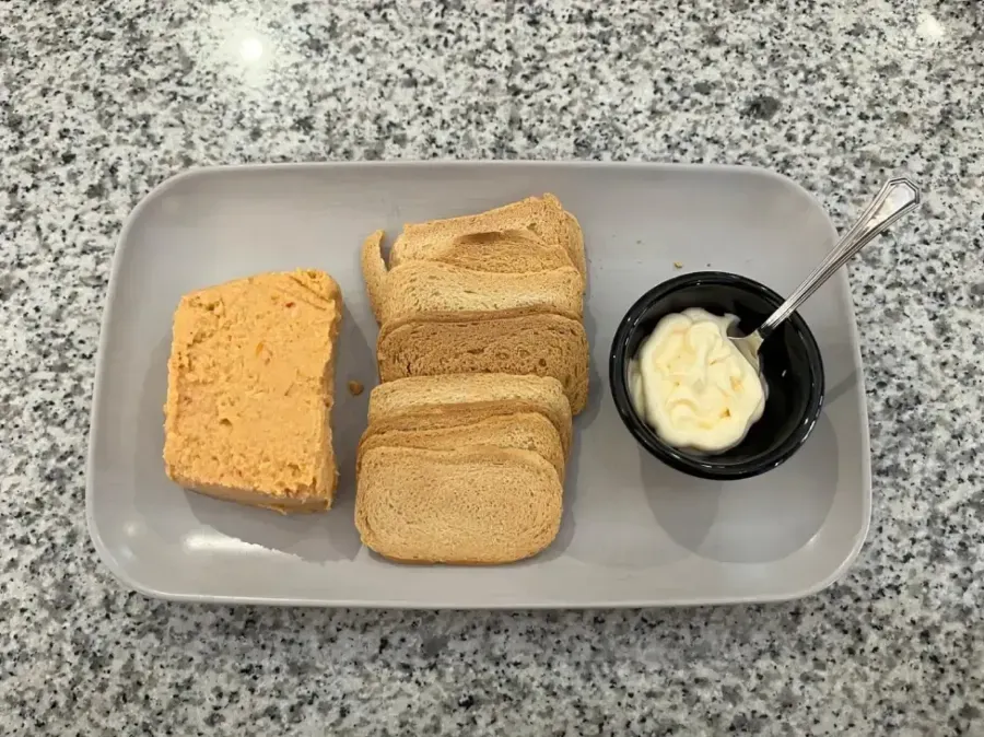 Bandeja con rebanadas de pan, mantequilla para untar y una cuchara sobre una encimera moteada.