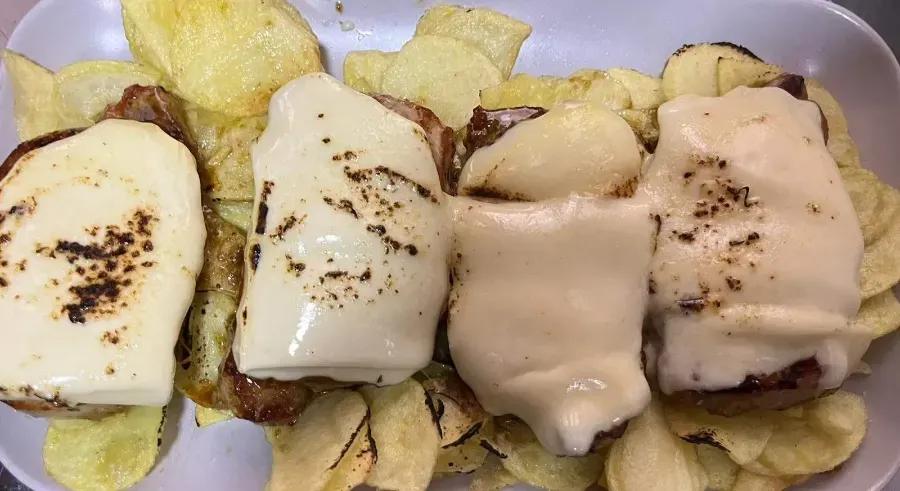 Bandeja de patatas cubiertas con queso fundido y salsa cremosa, con especias negras por encima.