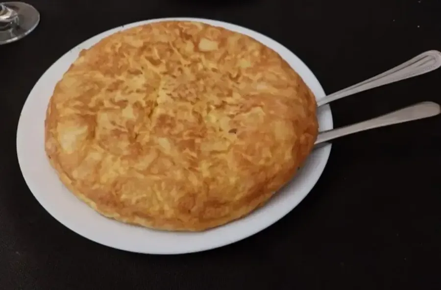 Tortilla simple en un plato blanco con dos tenedores sobre una mesa oscura.