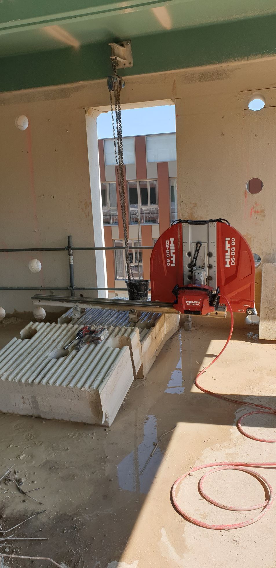 Un chantier de construction avec une grande scie rouge qui découpe des blocs de béton.