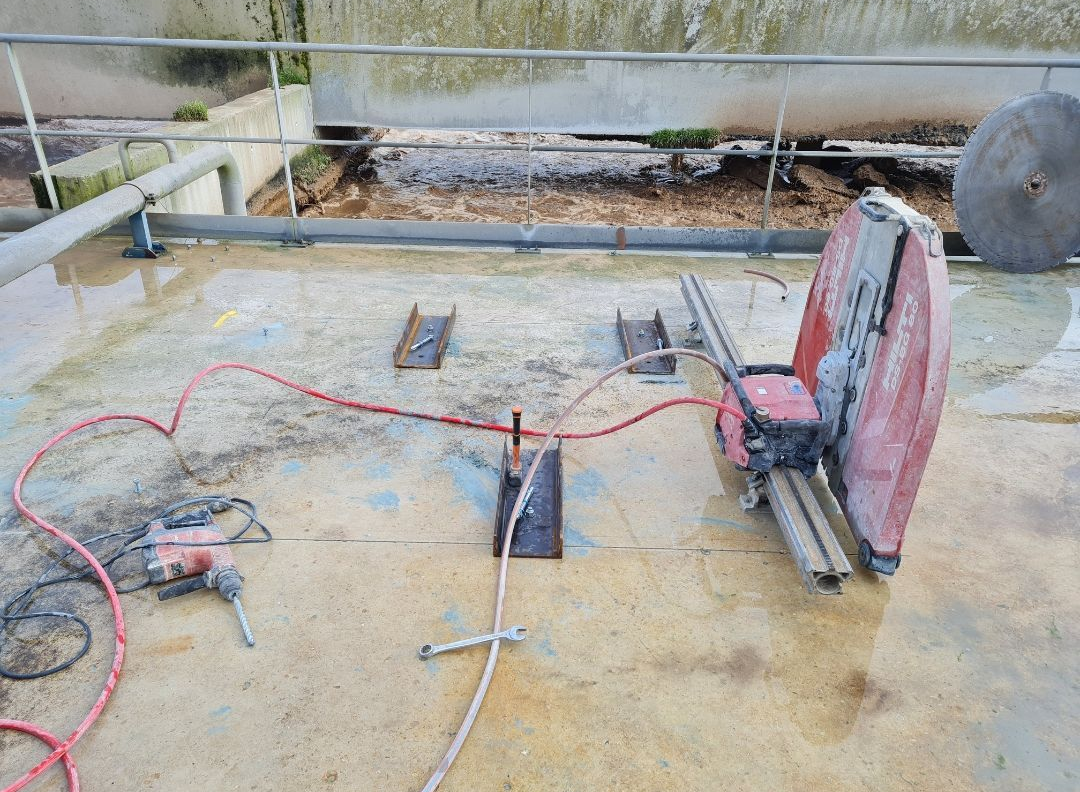 Scie à béton et perceuse sur béton frais, avec supports métalliques.