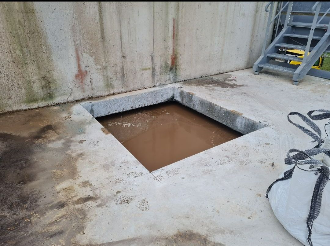 Fosse en béton contenant un liquide brunâtre, escalier adjacent.