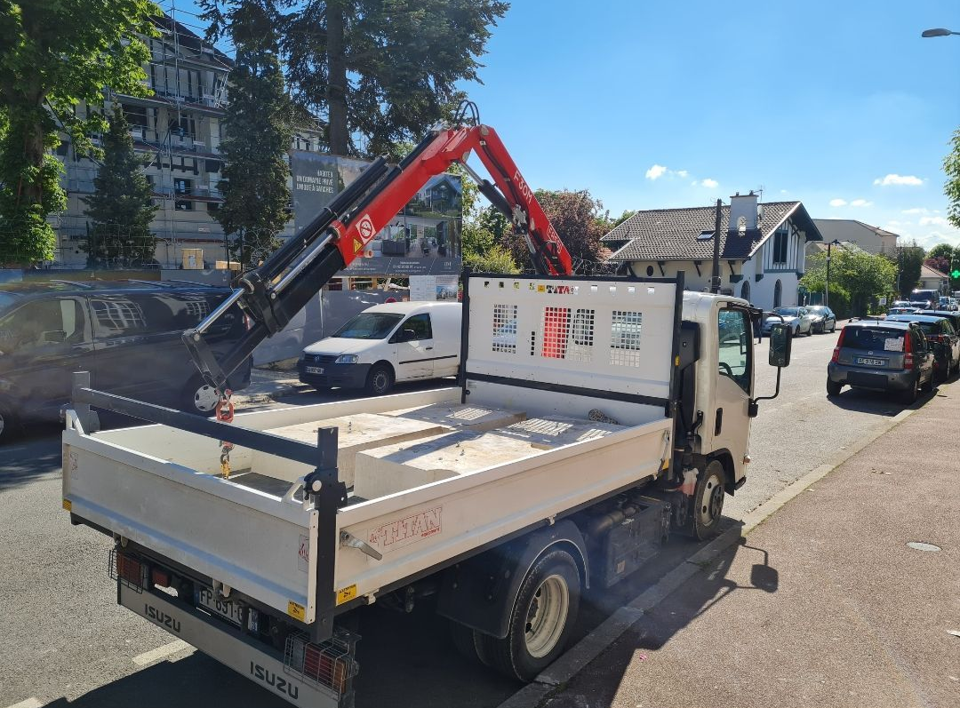 Un camion blanc équipé d'une grue charge des matériaux dans une rue ensoleillée.