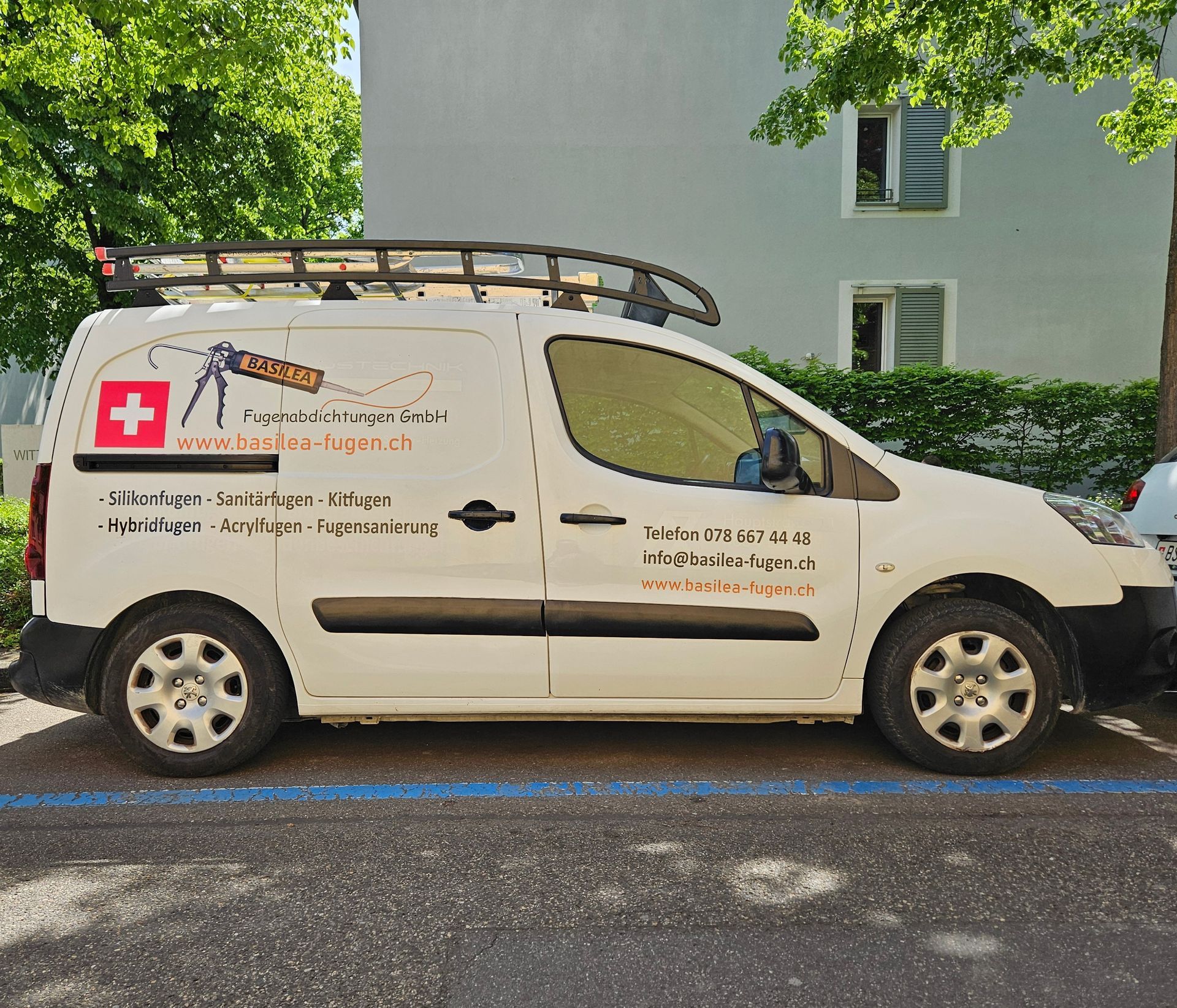 Ein weißer Lieferwagen mit einem roten Kreuz an der Seite steht auf einem Parkplatz