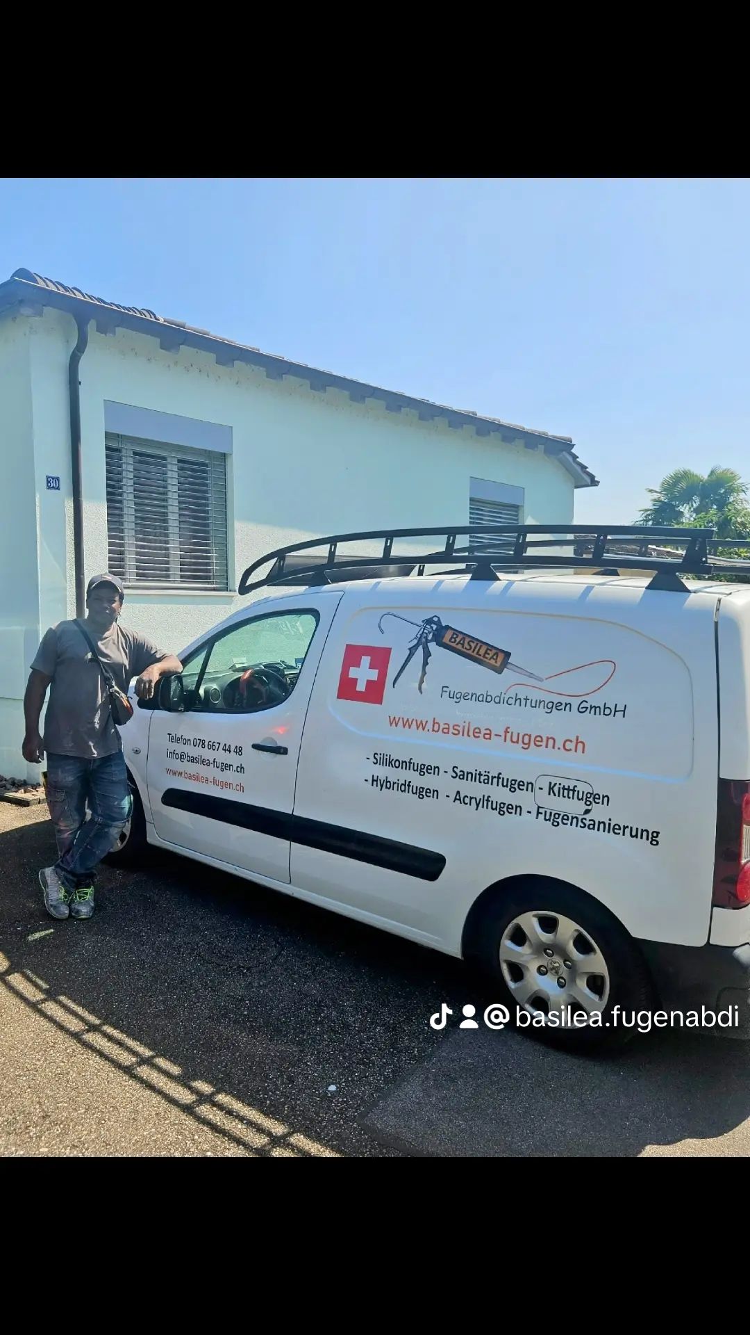 Ein Mann steht neben einem weißen Lieferwagen vor einem Gebäude.