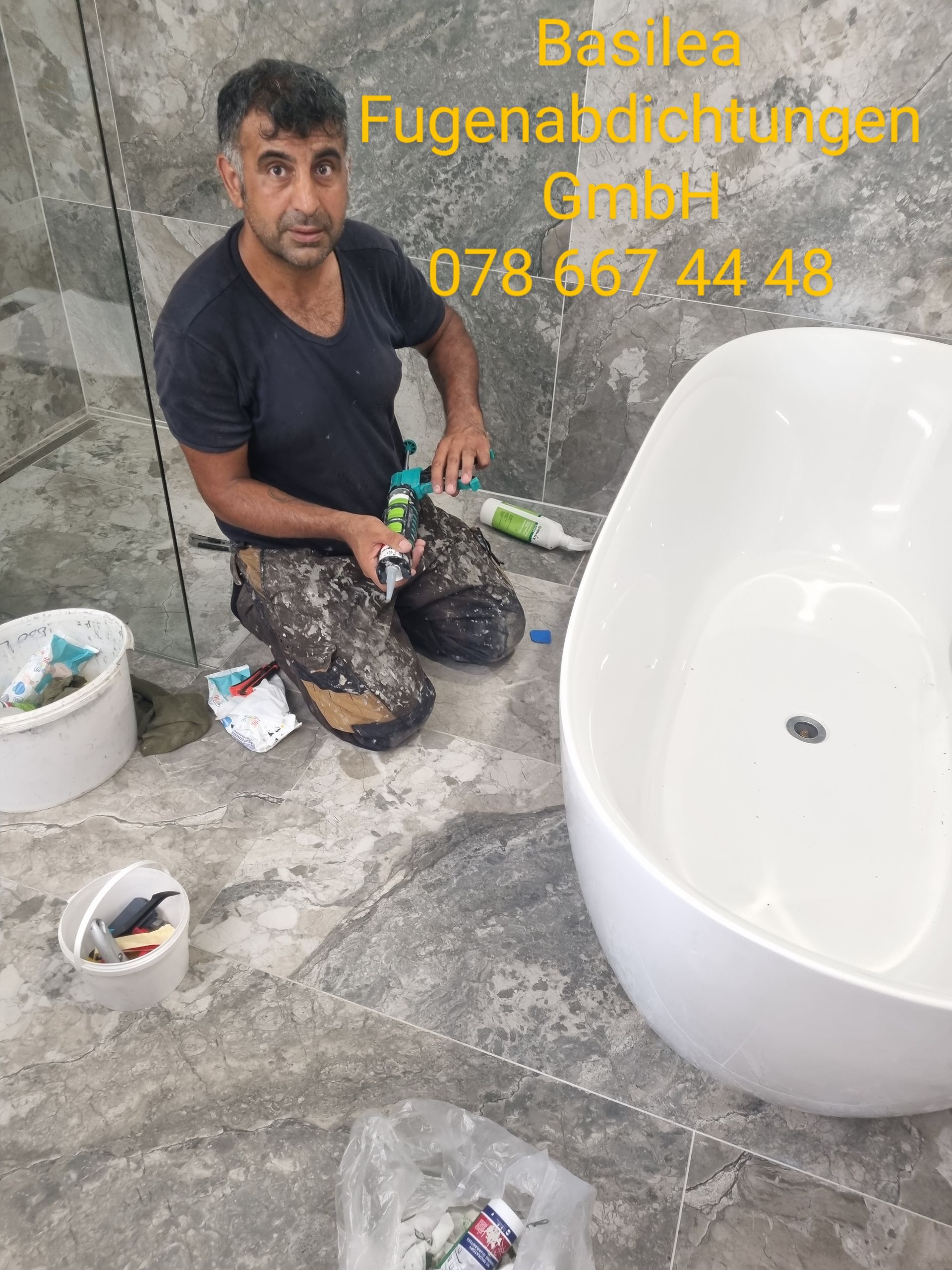 Ein Mann kniet neben einer Badewanne in einem Badezimmer.