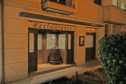 Entrada del restaurante con puertas de madera, iluminada por la noche, cartel beige 