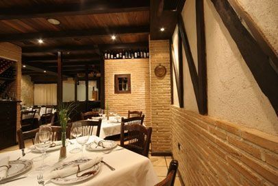 Interior de restaurante con paredes de ladrillo, vigas de madera, mesas preparadas para cenar.