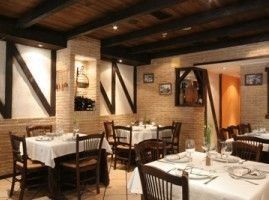 Interior de restaurante con vigas de madera, mesas con manteles blancos y paredes de ladrillo.