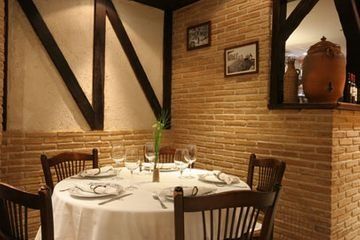 Acogedor juego de mesa de restaurante para cenar, con mantel blanco y sillas de madera, paredes de ladrillo.