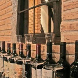 Botellas de vino en un estante con copas, fondo de pared de ladrillo.