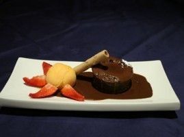 Pastel de lava de chocolate con helado, fresas y oblea en un plato blanco.