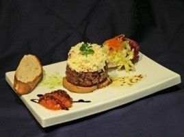 Un plato de tartar de carne gourmet con crutones y guarniciones en un plato rectangular blanco.
