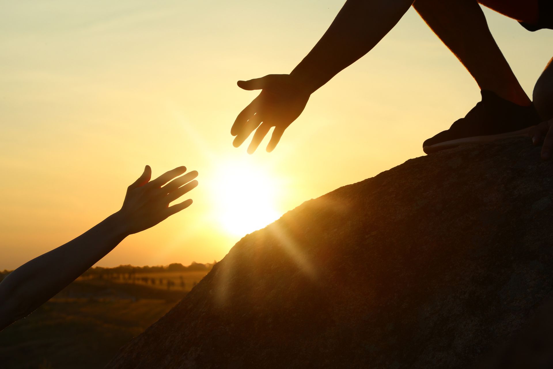 Des mains se tendent l'une vers l'autre au coucher du soleil, offrant de l'aide.