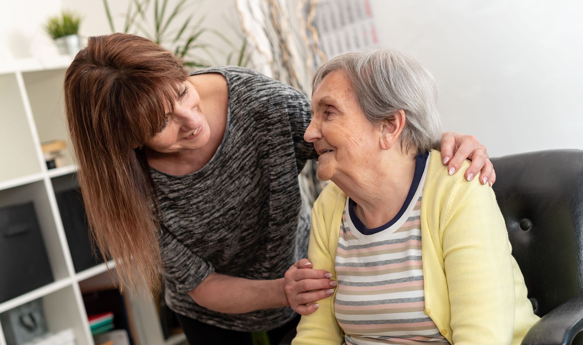 Une femme réconforte une femme âgée à l'intérieur ; toutes deux sourient, le bras de la femme autour des épaules de la personne âgée.
