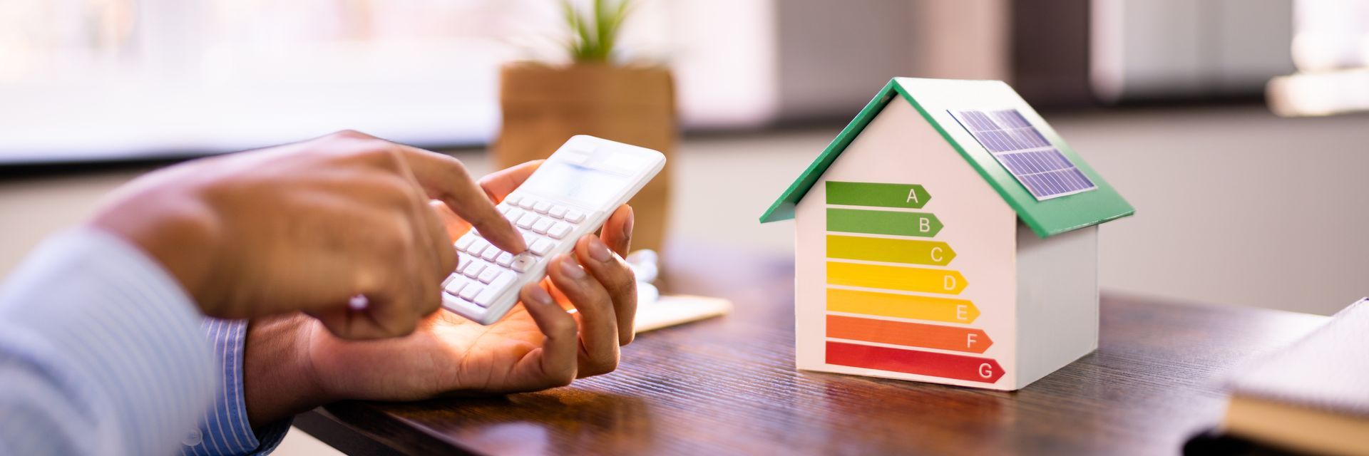 Calculatrice tenu dans des mains face à une maison avec une frise de DPE
