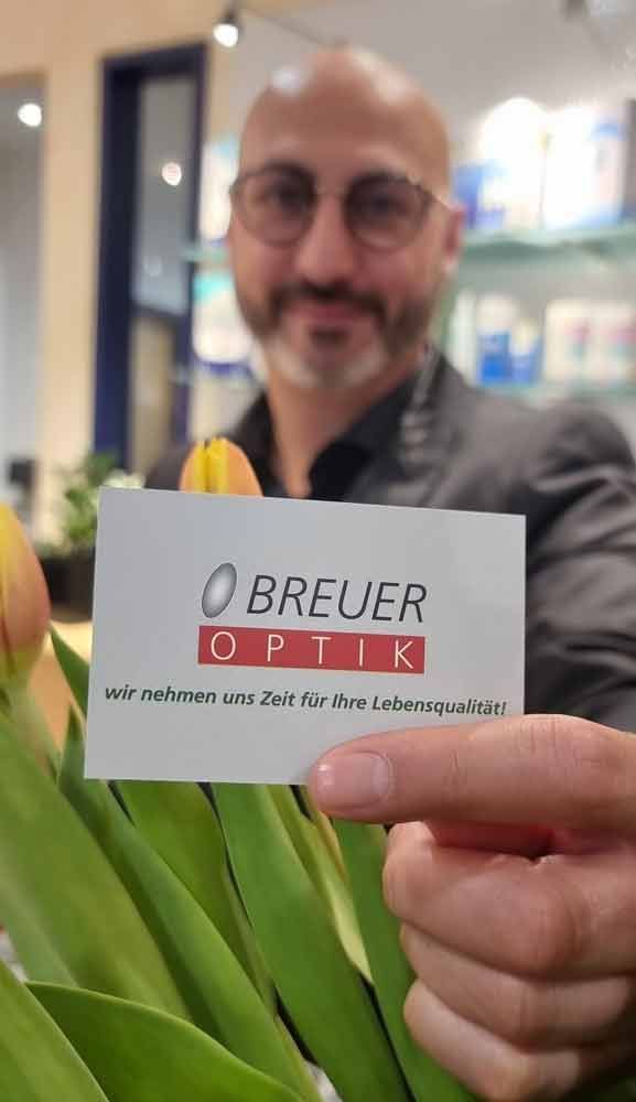 ein mann hält eine visitenkarte für breuer optik in der hand .
