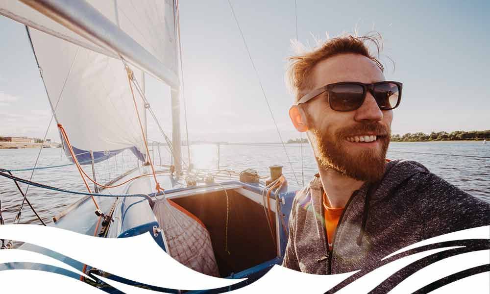 Ein Mann mit Bart und Sonnenbrille macht ein selfie auf einem Segelboot .