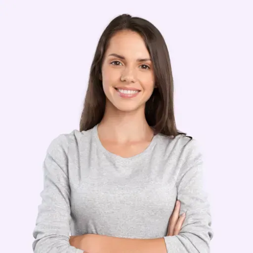Mujer de cabello largo castaño sonriendo, con los brazos cruzados y vistiendo una camisa gris de manga larga.