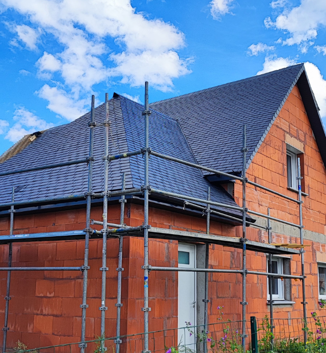 Une maison en briques est en construction avec des échafaudages autour.