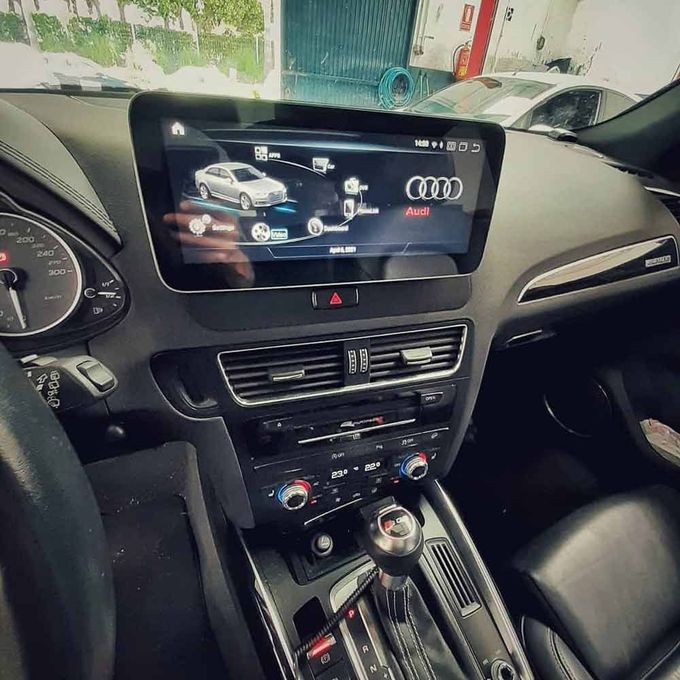 Interior del coche con salpicadero Audi, pantalla de infoentretenimiento, consola central y palanca de cambios automática.