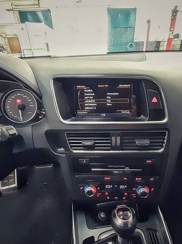 Tablero interior del automóvil con pantalla de infoentretenimiento, controles de climatización y palanca de cambios visibles.
