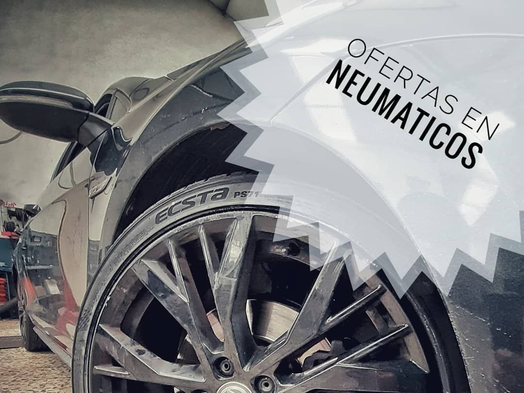 Rueda de coche en un garaje con un cartel blanco que dice “OFERTAS EN NEUMATICOS” sobre el neumático.