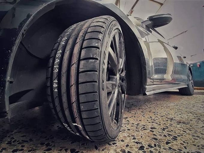 Primer plano del neumático delantero y la rueda de un coche deportivo negro sobre una carretera mojada.