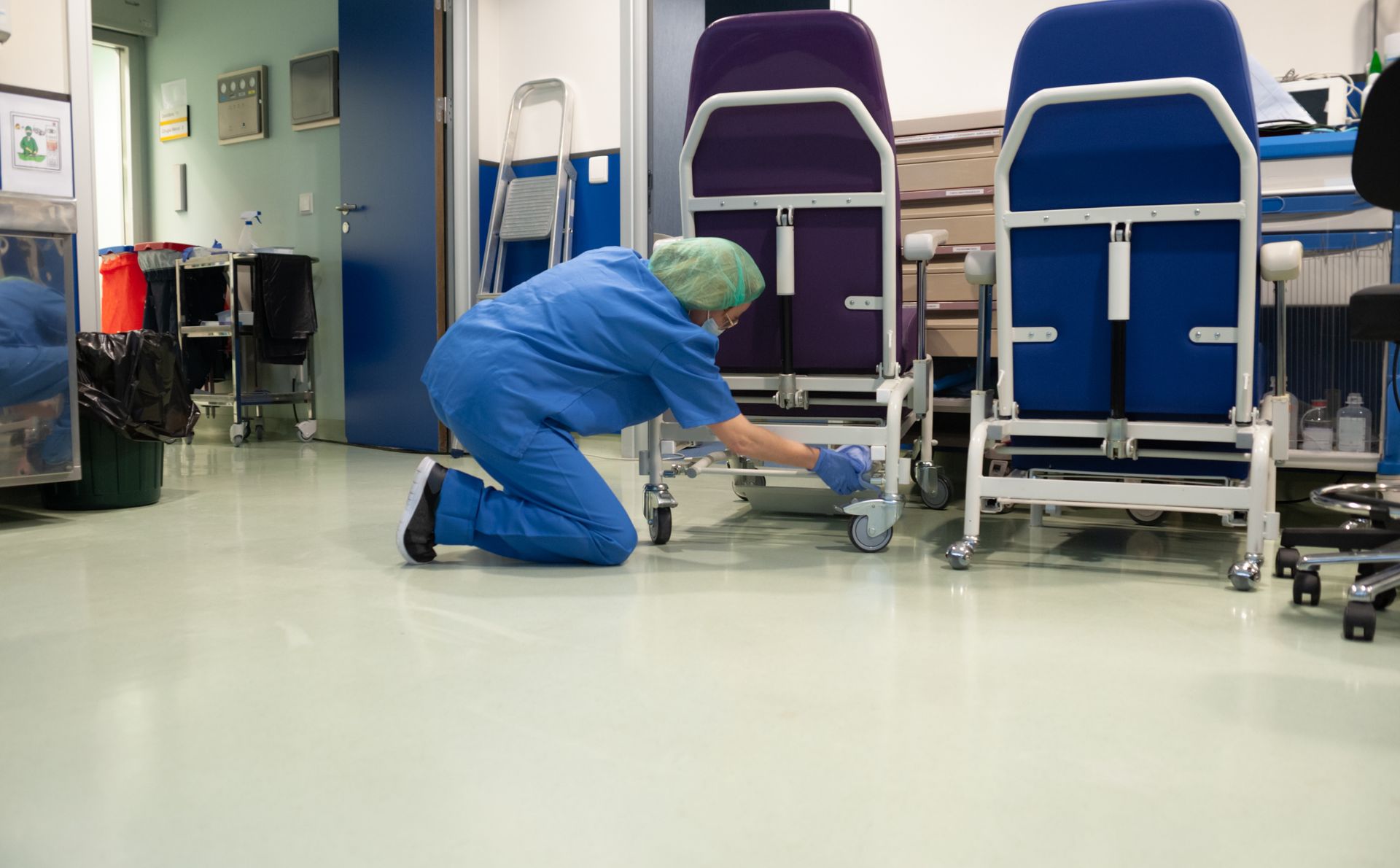 Agent en uniforme bleu nettoyant le sol à côté du matériel de l'hôpital