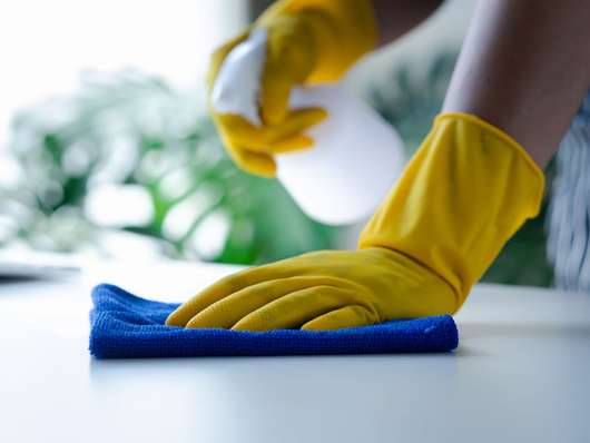 Main gantée de jaune essuyant une surface avec un chiffon bleu près d'un vaporisateur