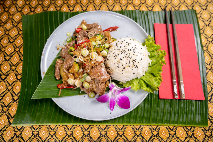 Ein Fleischgericht mit Reis angerichtet auf einem Teller mit Stäbchen auf einer roten Serviette im Thai Restaurant Zug.