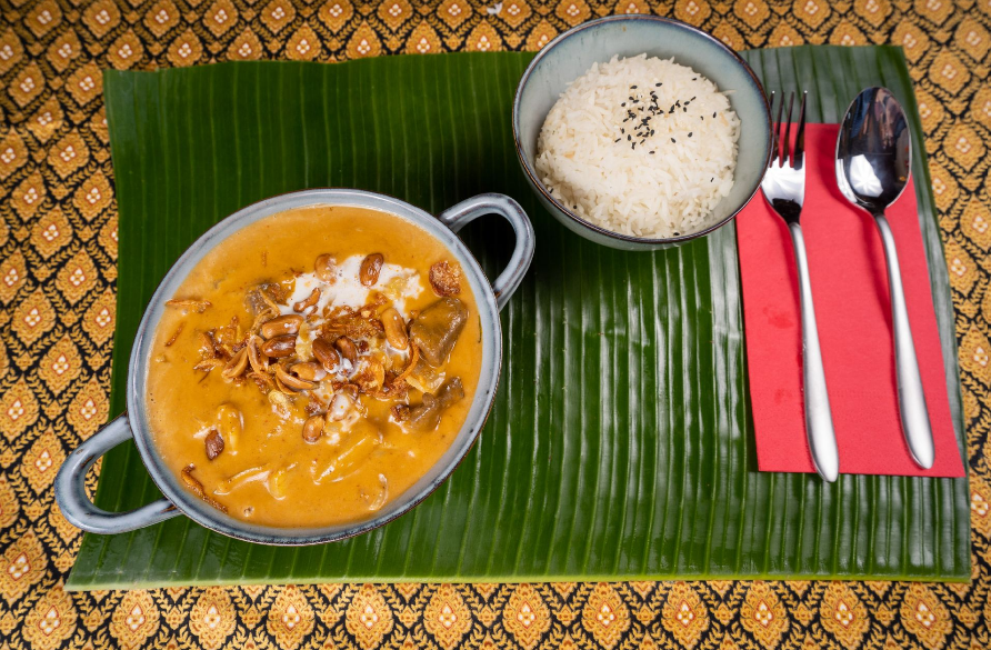 Massaman Curry angerichtet in einer Schüssel mit Besteck auf einer roten Serviette im Thai Restaurant Zug.