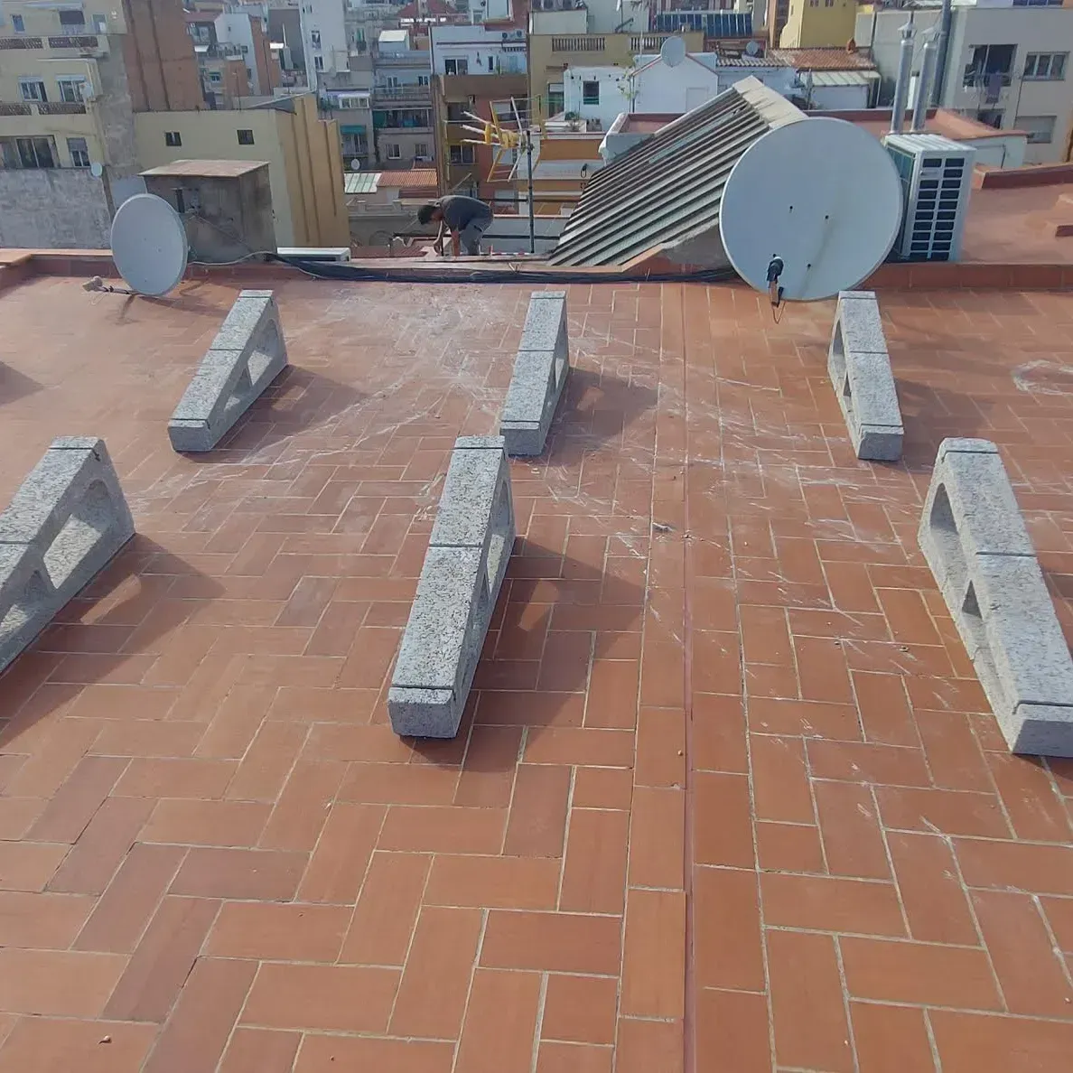 Azotea con tejas de terracota, soportes de hormigón y dos antenas parabólicas con vistas a la ciudad