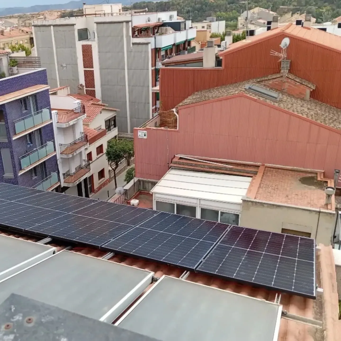 Paneles solares en una azotea con vistas a edificios densamente agrupados en un día nublado