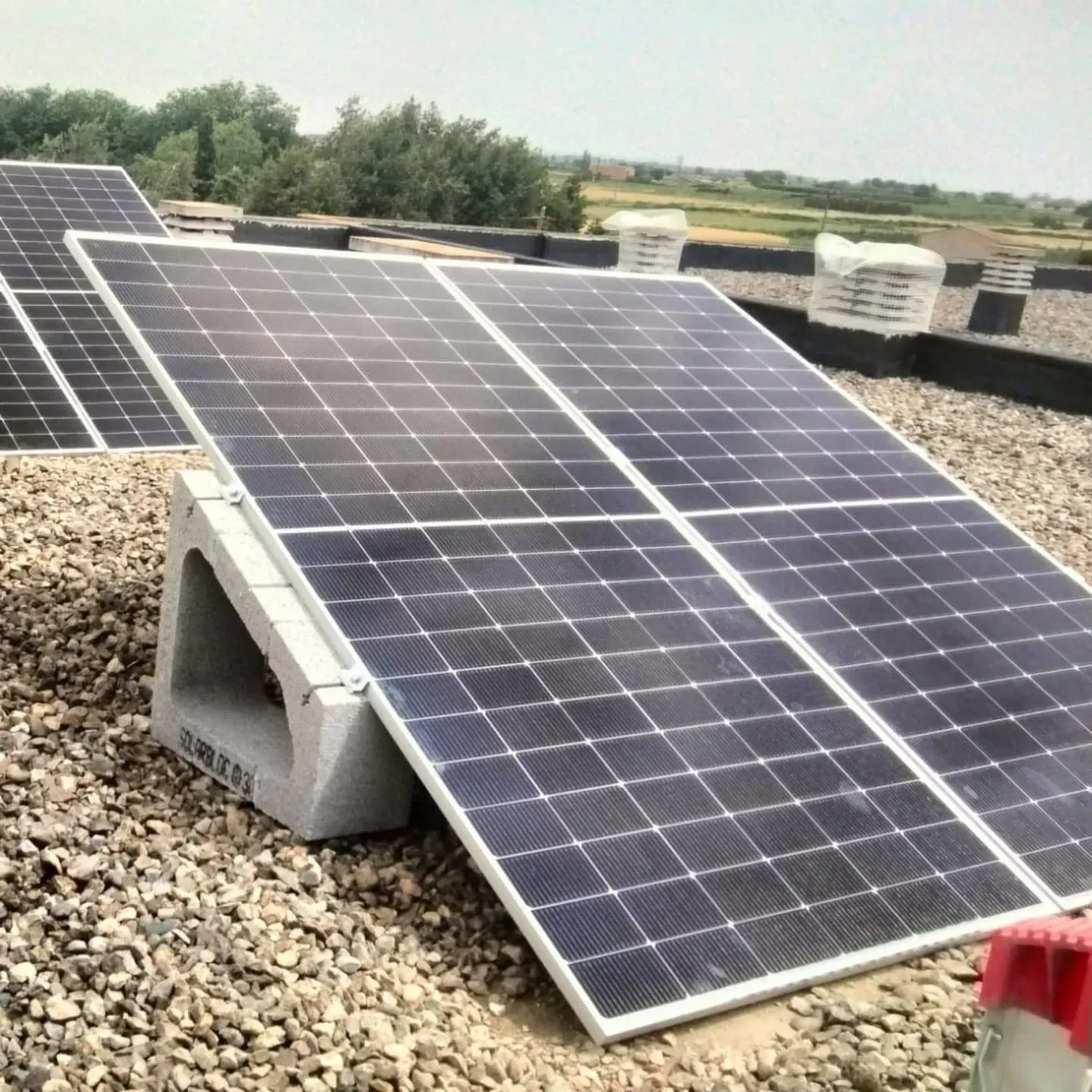 Paneles solares montados sobre bloques de hormigón en una azotea cubierta de grava, bajo un cielo despejado