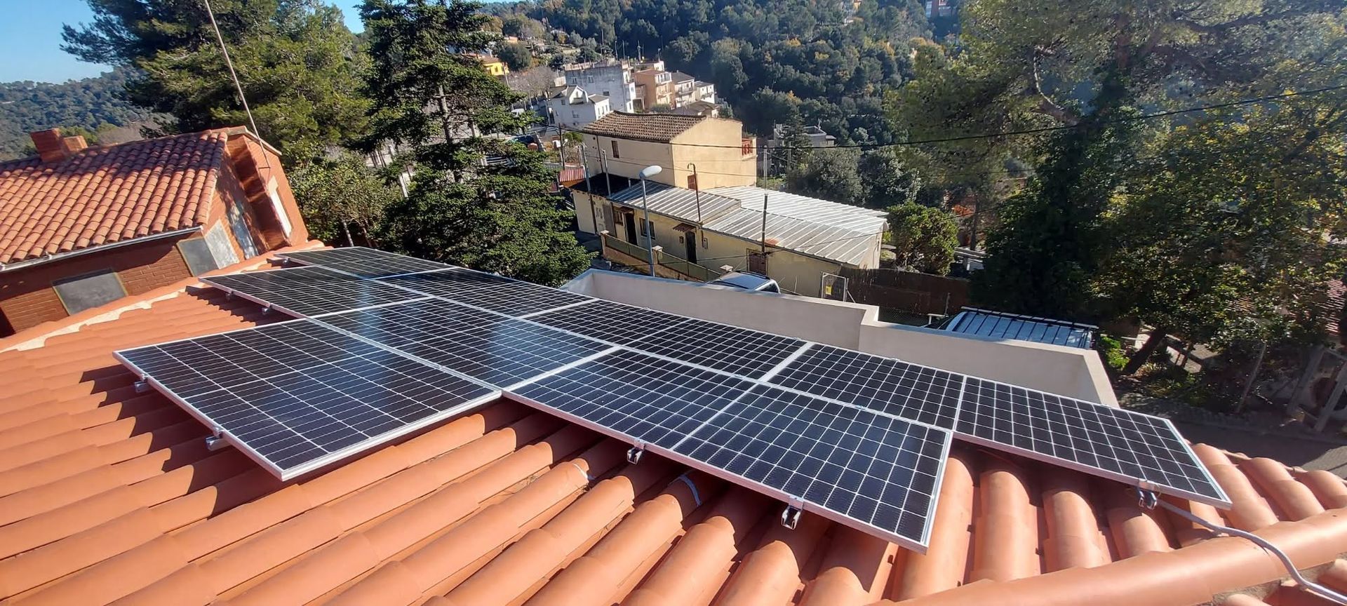 Paneles solares instalados en un tejado de terracota con vistas a árboles y casas vecinas