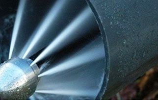 Primer plano de una boquilla metálica que rocía agua en forma de abanico sobre una superficie oscura.