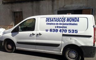 Furgoneta blanca de servicio con el letrero de la empresa de fontanería “Desatascos Monda” estacionada junto a un edificio.