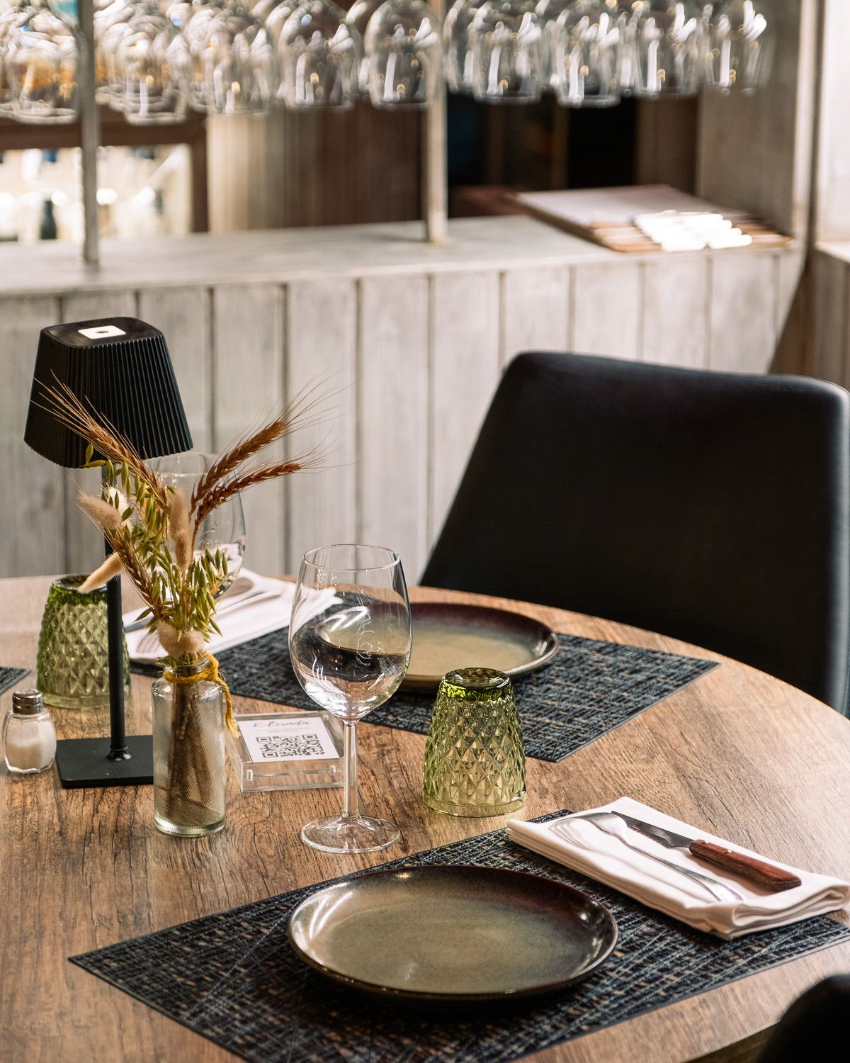 Una mesa de madera con platos, copas de vino y un jarrón con flores encima.
