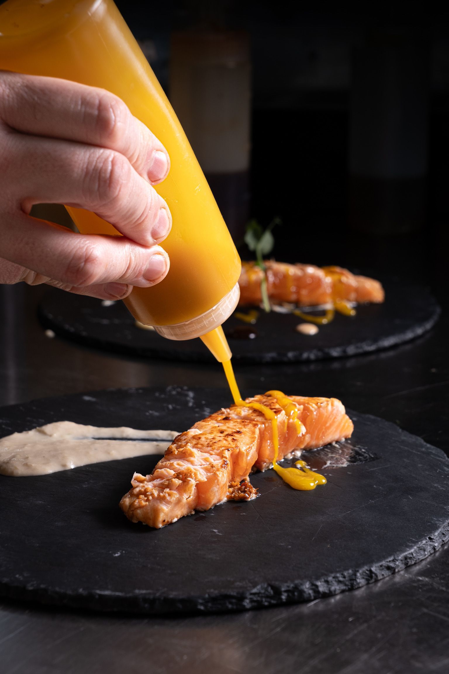 Una persona está vertiendo salsa sobre un trozo de salmón en un plato.