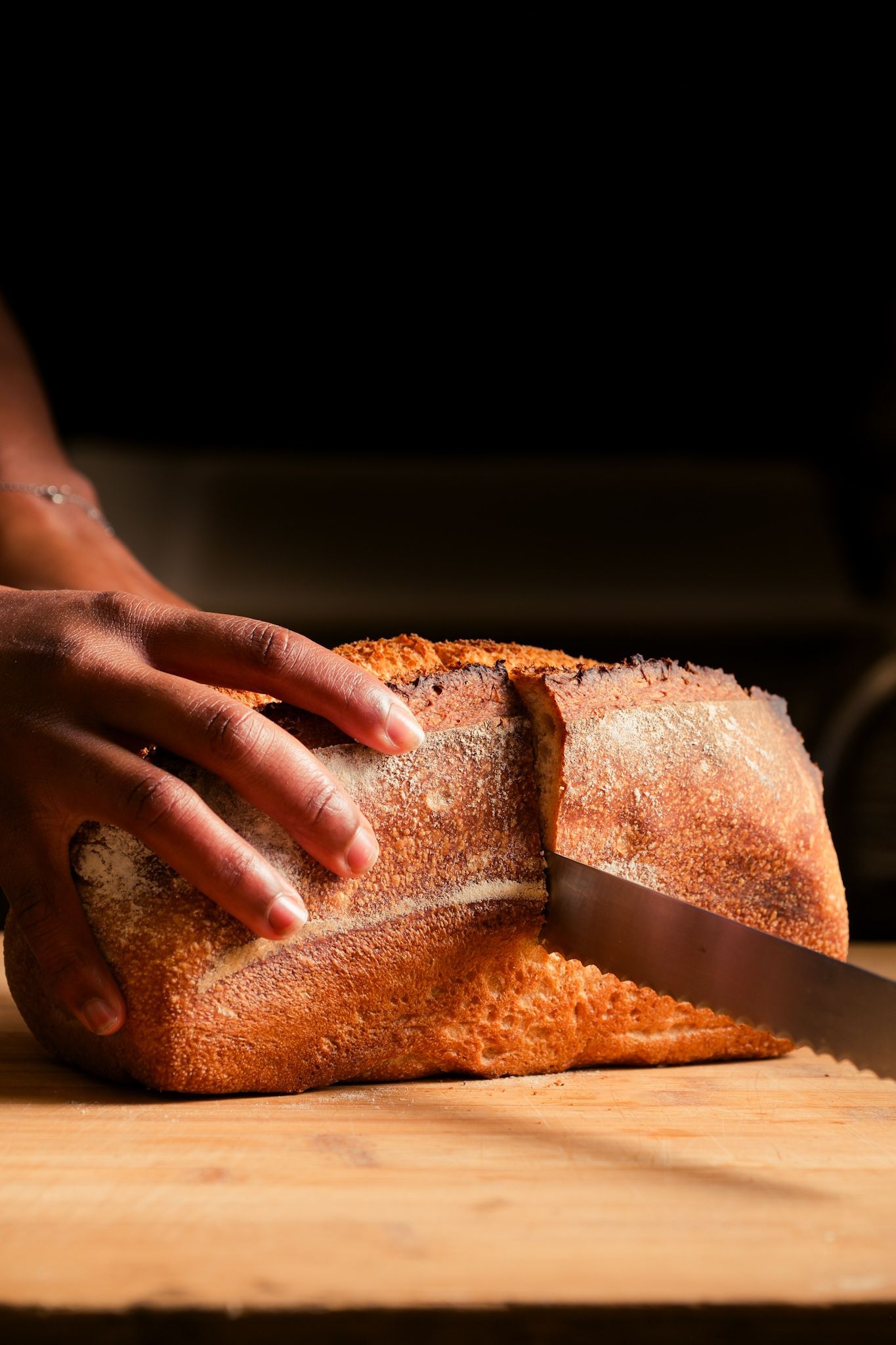 Una persona está cortando una hogaza de pan en una tabla de cortar.