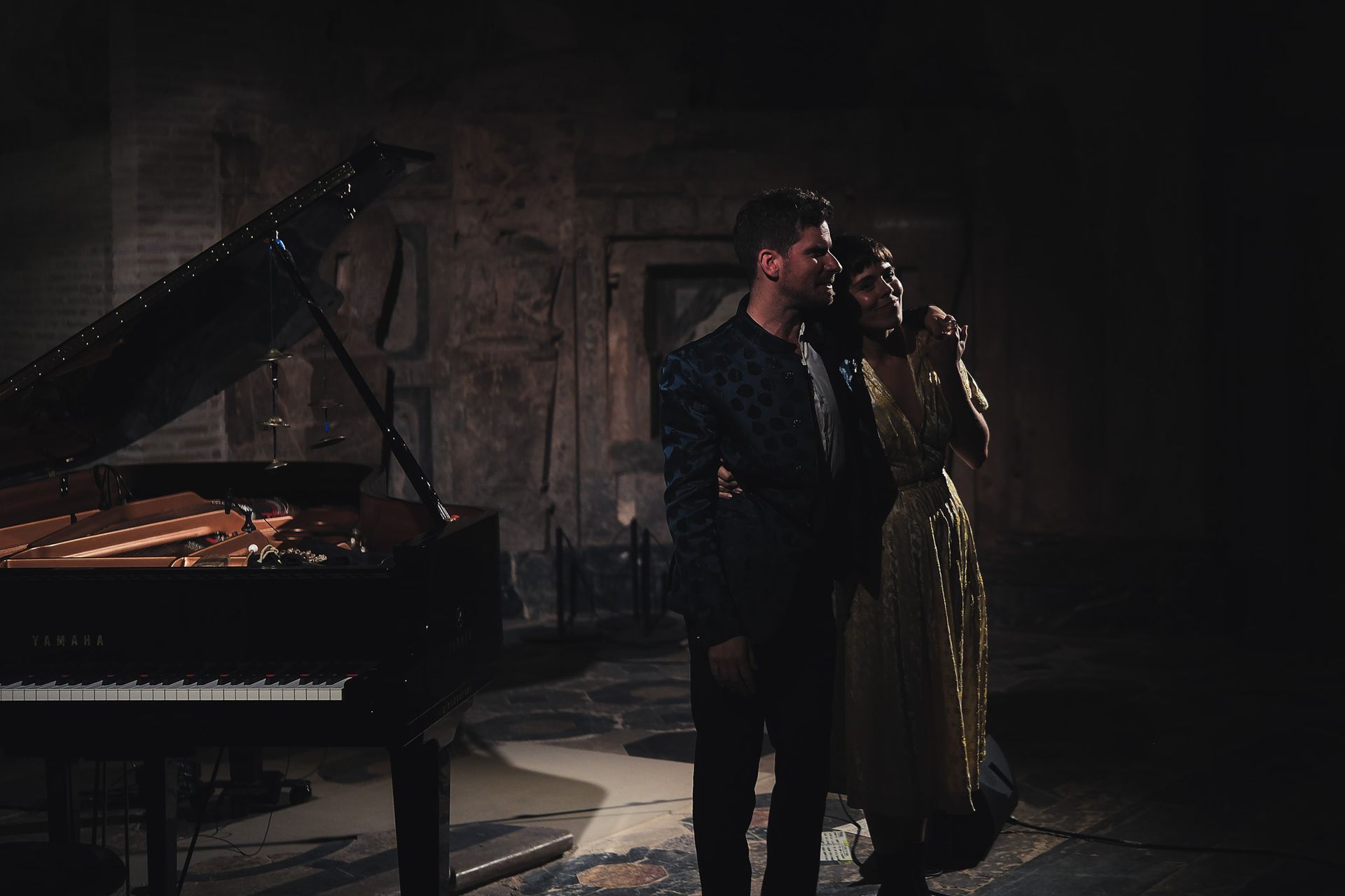 Un hombre y una mujer están de pie junto a un piano en una habitación oscura.