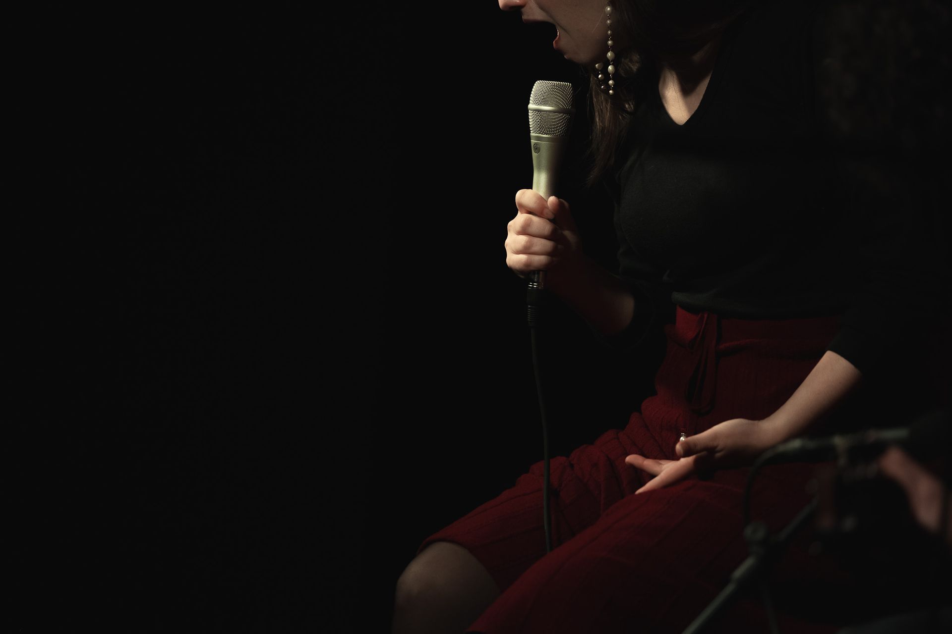 Una mujer cantando con un micrófono en una habitación oscura.