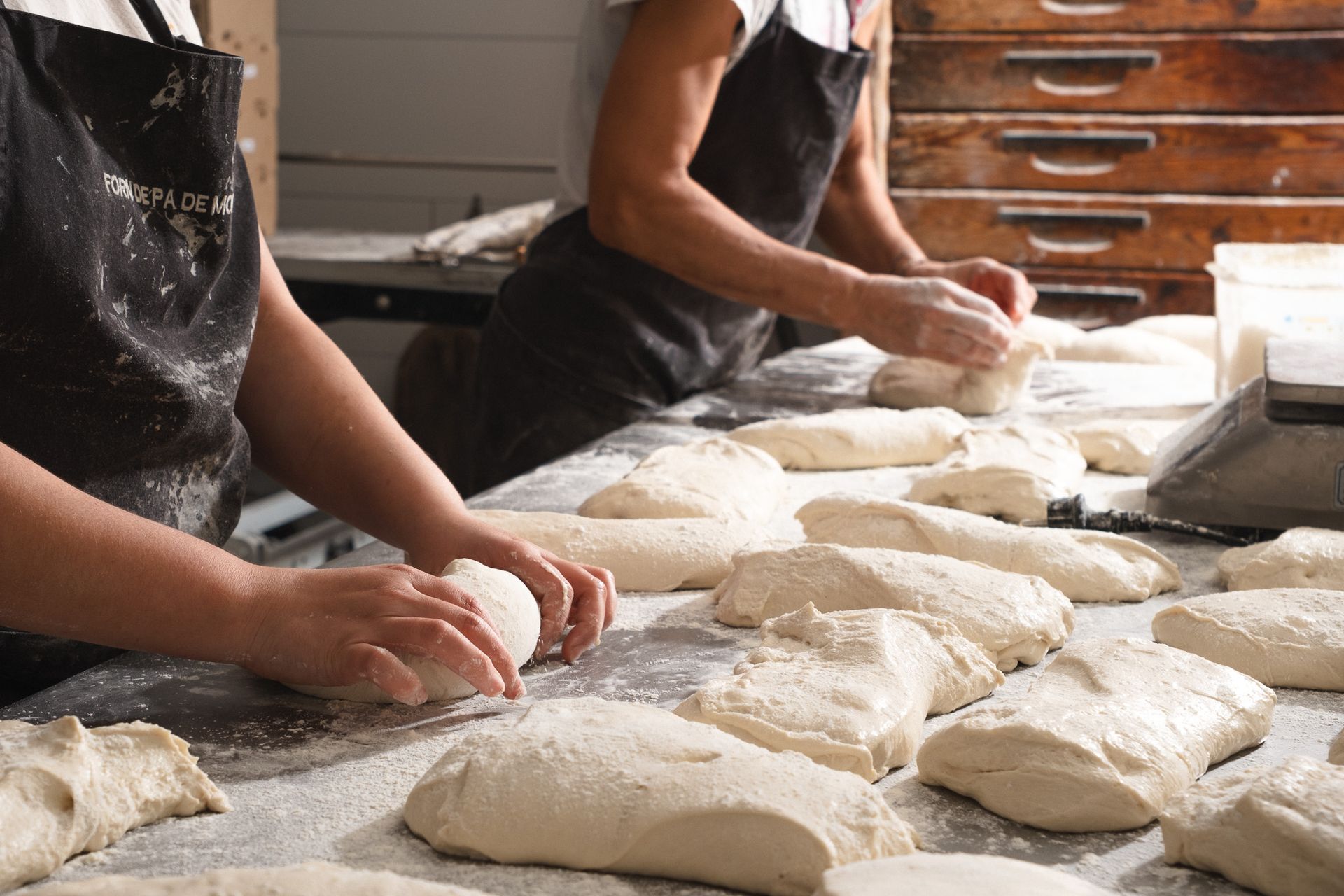 Dos personas están amasando masa en una mesa en una panadería.