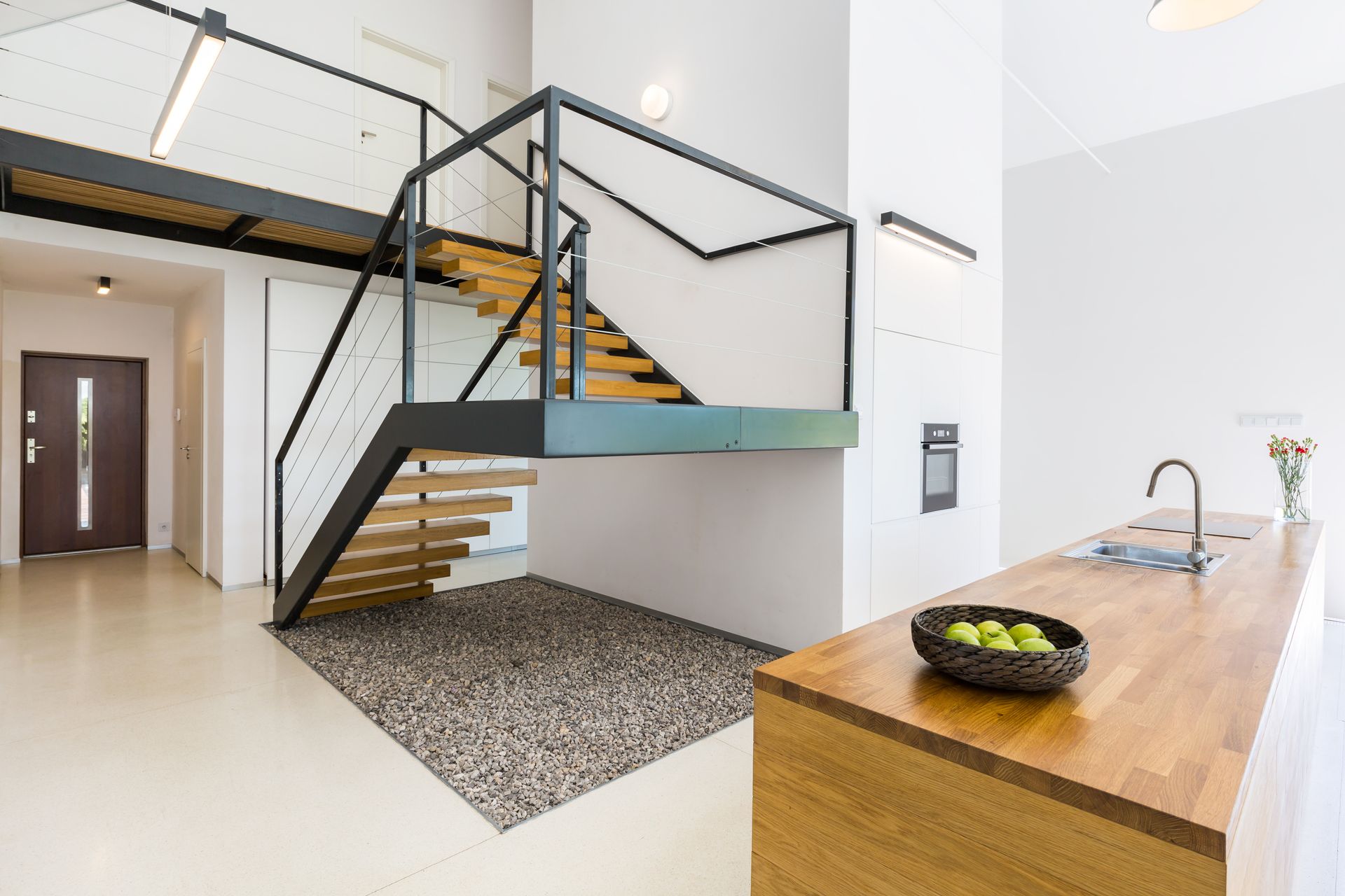 Intérieur moderne avec escalier suspendu, garde-corps en verre et îlot de cuisine en bois avec évier