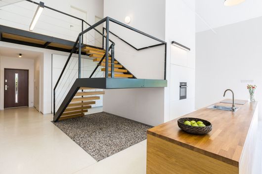 Intérieur moderne avec escalier suspendu, rampes noires et îlot en bois dans un espace ouvert et lumineux