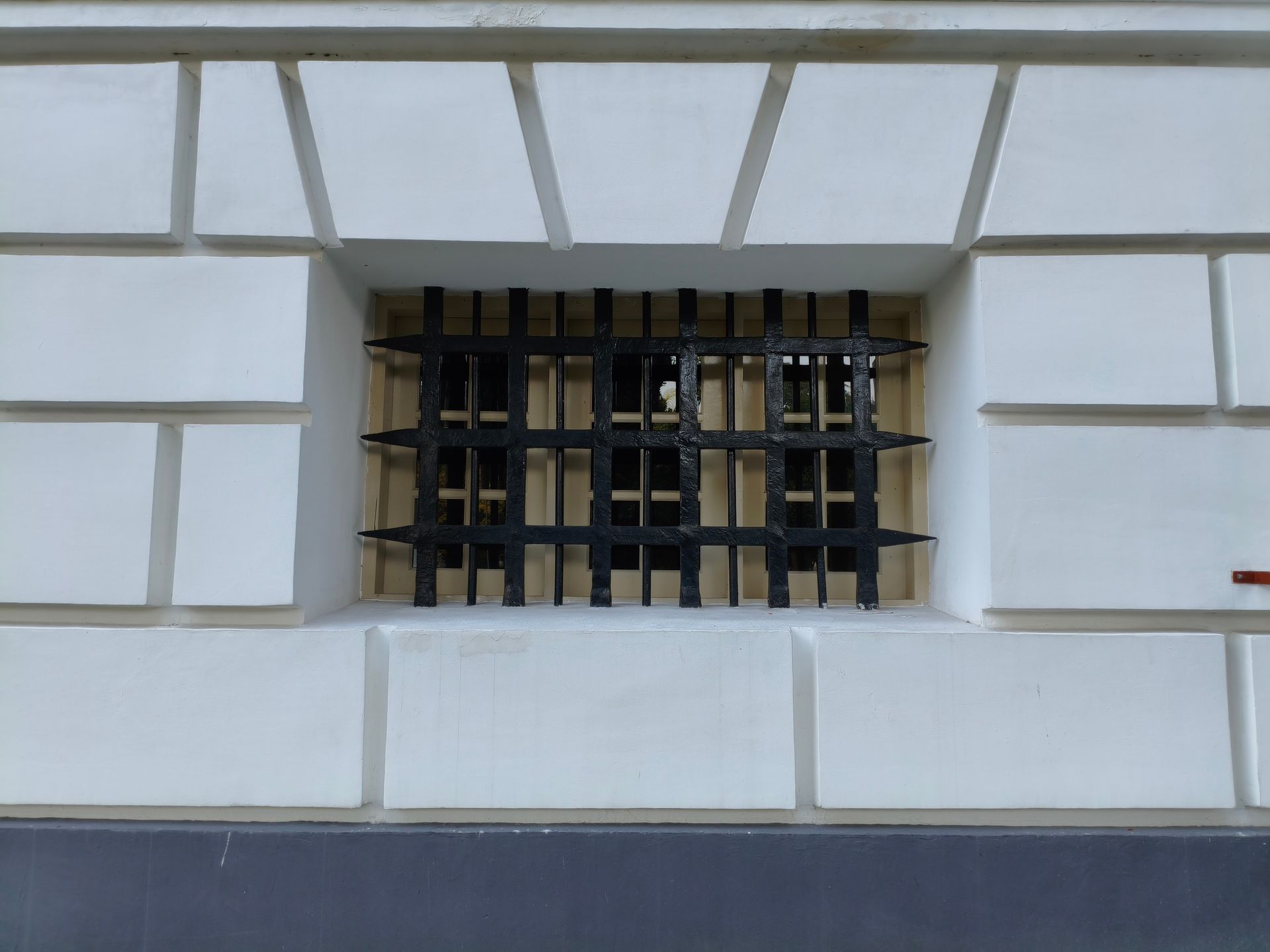 Mur blanc d'un bâtiment avec une petite fenêtre à barreaux au centre